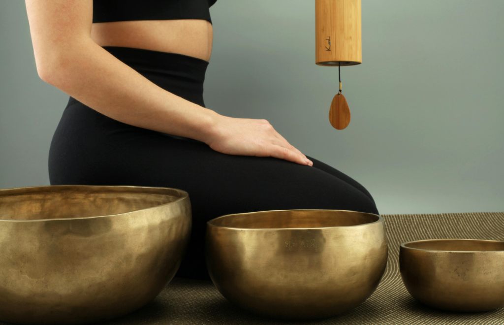 a woman sitting next to himalayan singing bowls for sound therapy