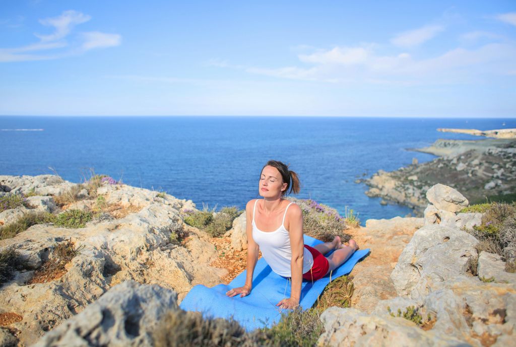 a woman doing yoga on a clifftop with the sea in the background. Solo travel is a trending way to market wellness travel.