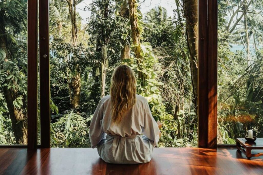 a woman sitting on a wooden floor facing away towards a forest